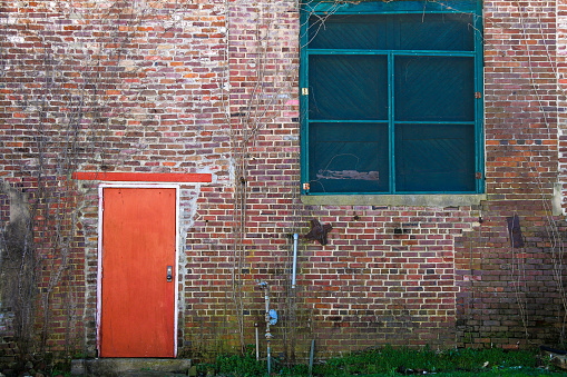 A vintage retro old red brick building alley wall with bright red door and green boarded up windows.