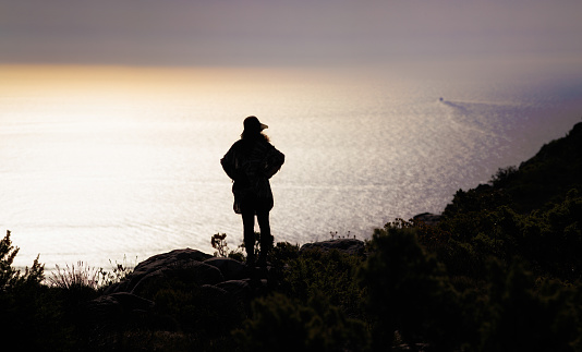 Panoramic back lit view of a female tourist looking at the view from the top of Table Mountain in Cape Town South Africa toward the Atlantic Ocean.
