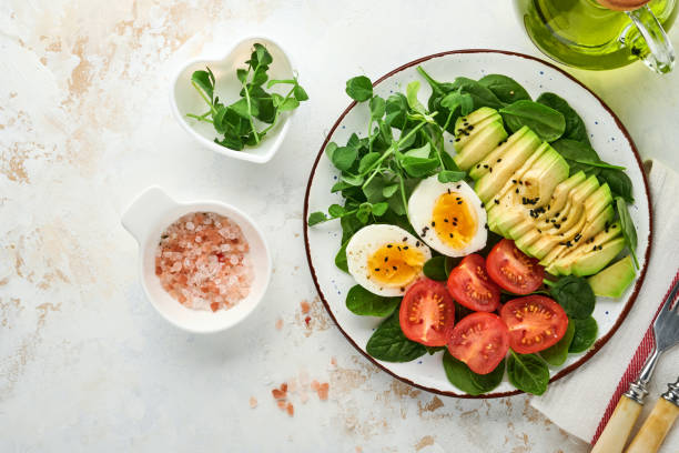 istock Avocado, cherry tomato, spinach and chicken egg, microgreens peas and black sesame seeds fresh salad in bowl on white stone table background. Healthy breakfast food concept. Top view. 1323368979