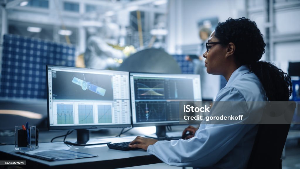 Female Engineer uses Computer to Analyse Satellite, Calculate Orbital Trajectory Tracking. Aerospace Agency International Space Mission: Scientists Working on Spacecraft Construction. Over Shoulder Engineer Stock Photo