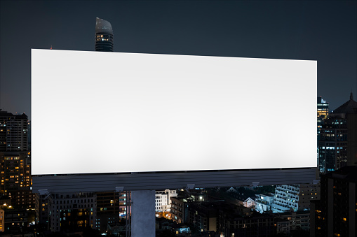 Blank white road billboard with Bangkok cityscape background at night time. Street advertising poster, mock up. Front view. The concept of marketing communication to promote idea.