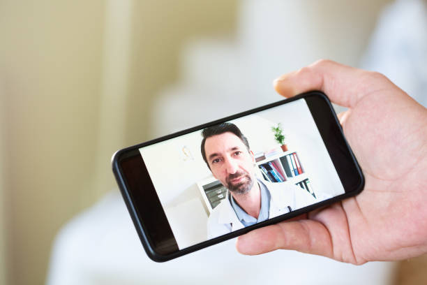 istock Telemedicine: hand holding mobile phone during video call with doctor 1323373433