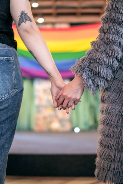 szene von 2 frauen halten hände und die homosexuell stolz flagge im hintergrund - pride lgbtqi veranstaltung stock-fotos und bilder