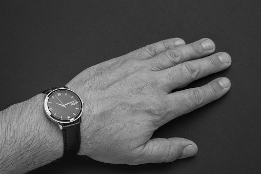 A man's hand with a wrist watch with hands on a black background. A fashionable and stylish men's accessory.