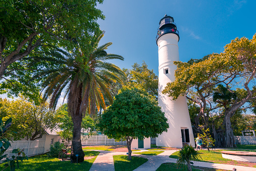 Key West, USA - 04.30.2017: Old lighthouse and its surroundings of old, white, wooden houses and green trees in Key West, Florida on a beautiful sunny day. Tourism in tropical paradise. Sunshine state.