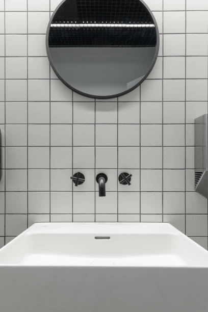 istock Modern public restroom minimal interior with metro style white tiles, round mirrors, black ceiling 1323385380