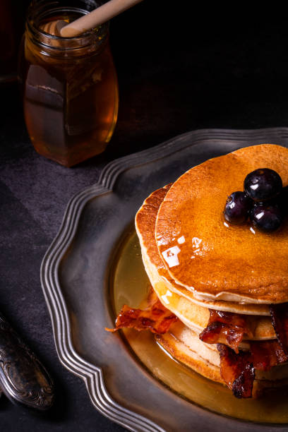 istock Fresh homemade pancake stack with crispy organic bacon and blueberry fruit butter drippings honey maple syrup for tasty sweet morning breakfast with American traditional authentic style 1323389411