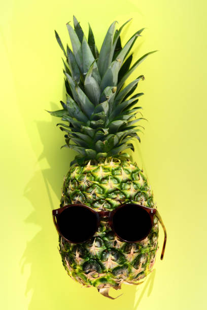 A ripe pineapple with sunglasses against a yellow background