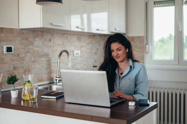 istock Woman using a laptop and airpods while sitting in the kitchen 1323400251