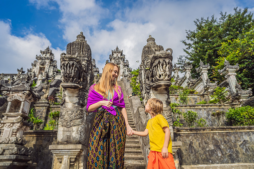 Mother and son tourists on background of Three stone ladders in beautiful Pura Lempuyang Luhur temple. Summer landscape with stairs to temple. Paduraksa portals marking entrance to middle sanctum jaba tengah of Pura Penataran Agung, Bali. Traveling with children concept. Kids friendly place.