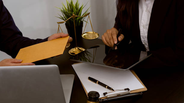 Businessman offers money to lawyer in office with laptop and scales of justice. Businessman offers money to lawyer in office with laptop and scales of justice. Personal Injury Lawyer stock pictures, royalty-free photos & images