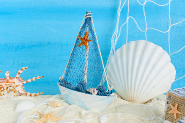 istock Ship, fishing net, seashells, starfish and chest on sand with copy space on blue textured backdrop. 1323419961