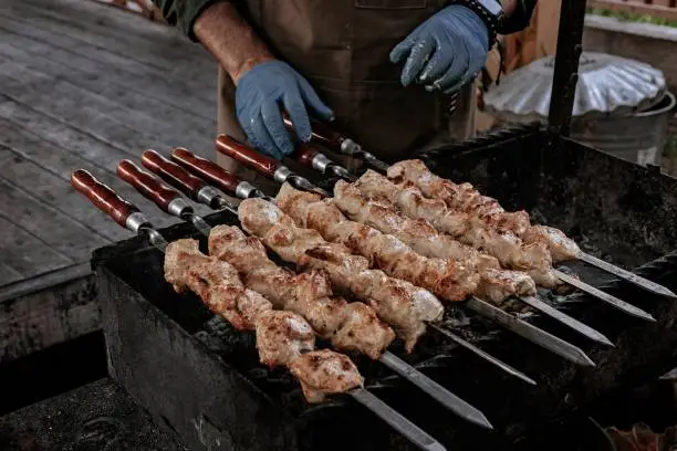 The chef prepares chicken shish kebab. Street food. Meat cooked over a fire, BBQ party in the backyard. Male hands in gloves hold steel skewers with delicious chicken shish-kebab