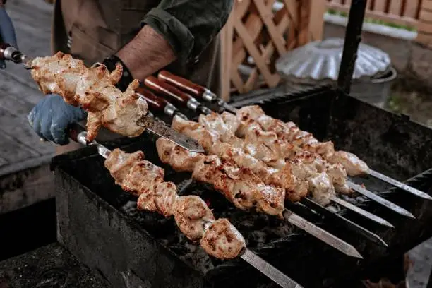 The chef prepares chicken shish kebab. Turkish Street food. Meat cooked over a fire, BBQ party in the backyard. Male hands in gloves hold steel skewers with delicious chicken shish-kebab