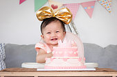 幸せとピンクの王女のケーキで彼女の最初の誕生日を祝うかわいいアジアの女の赤ちゃんの肖像画。