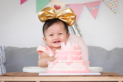 Portrait of cute asian baby girl celebrating her first birthday with pink princess cake with happiness.