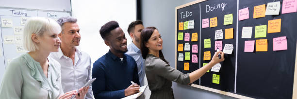 Group Of People Writing On Sticky Notes Side View Of Group Of People Writing On Sticky Notes Attached To Blackboard In Office scrum stock pictures, royalty-free photos & images