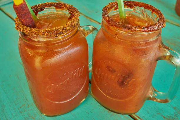 Michelada served in a mason glass with sweet tamarind and spicy garnish, on a greenish-blue wooden background stock photo