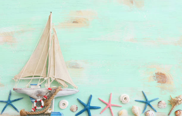 nautical concept with white decorative sail boat, seashells over wooden table and blue background