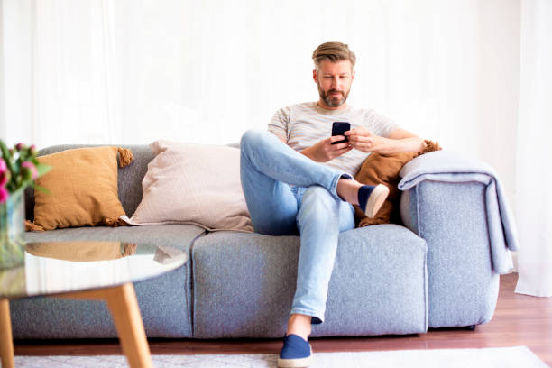 istock Handsome man wearing casual clothes while sitting on sofa and using his phone 1323439268