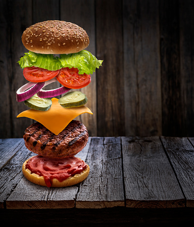 Burger layered ingredients as explosion flying open bun cheeseburger on rustic wooden table background