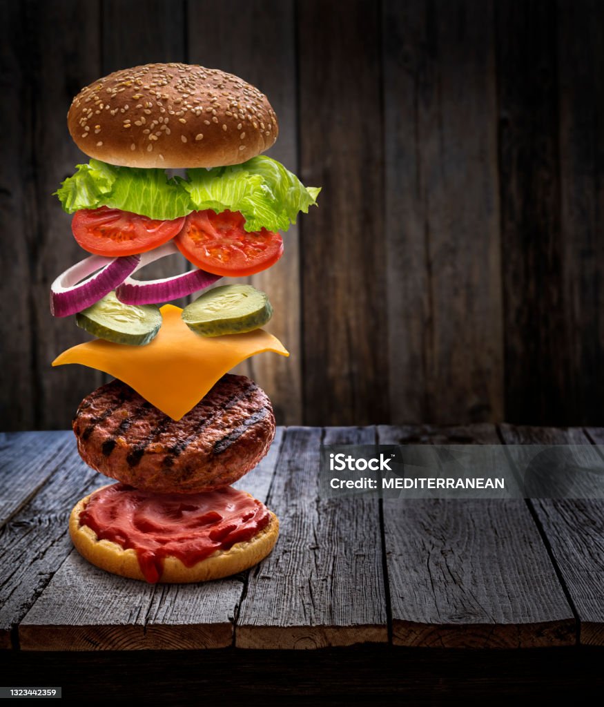 Burger layered ingredients as explosion flying open bun on rustic wooden table Burger layered ingredients as explosion flying open bun cheeseburger on rustic wooden table background Burger Stock Photo