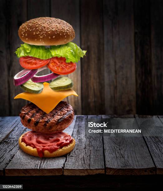 Burger Layered Ingredients As Explosion Flying Open Bun On Rustic Wooden Table Stock Photo - Download Image Now