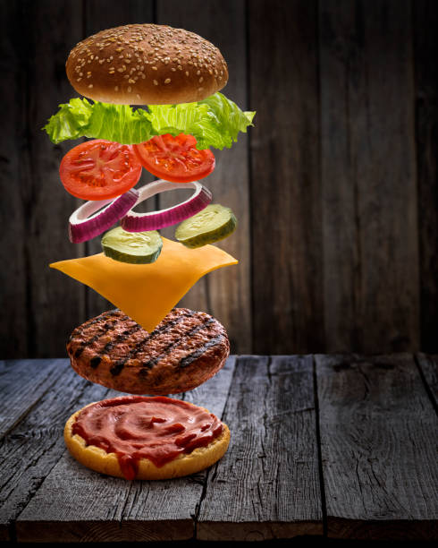 istock Burger layered ingredients as explosion flying open bun on rustic wooden table 1323442365
