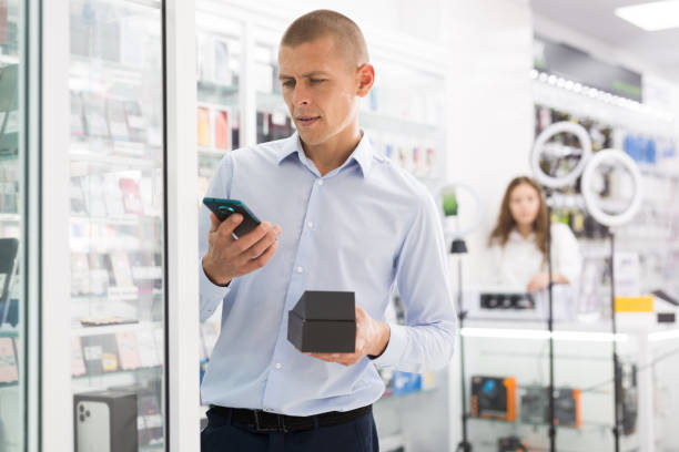 istock Smiling male holding mobile phone in the hand at electronics store 1323443118