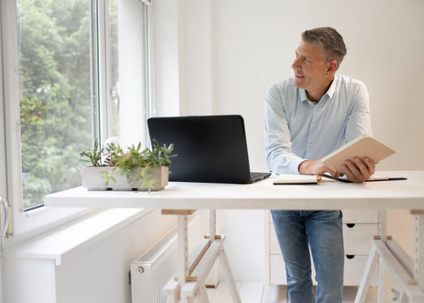 istock business man is standing behind high standing table and is working with his tablet 1323443493