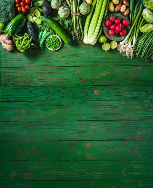 Photo of Vegan vegetables on green wooden table copy space