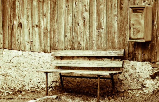 Empty wooden bench standing outdoors against a dark brick wall in sunlight