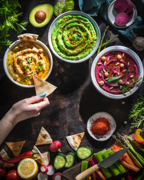 Hummus bowls of chickpeas, avocado and beetroot female hand dip with cut vegetables for dipping Hummus bowls of chickpeas, avocado and beetroot female hand dip with cut vegetables for dipping on dark wooden table background lebanese culture stock pictures, royalty-free photos & images