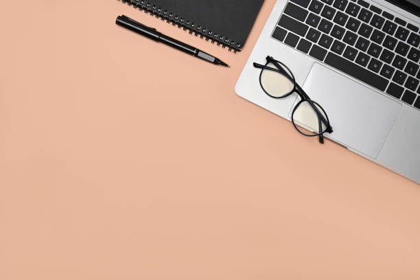 istock Above view laptop, glasses and notebook on cream background. 1323443881
