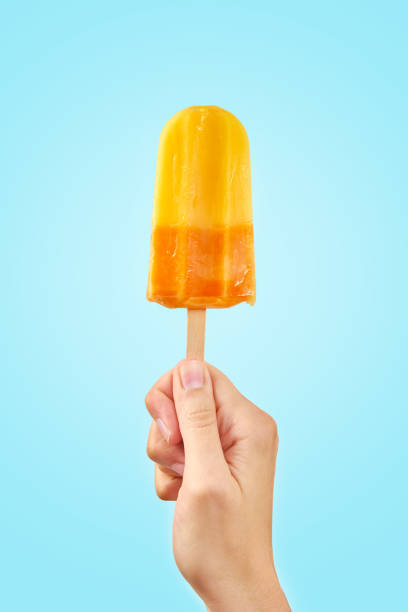 istock Yellow frozen fruit ice cream popsicle in hand on blue background 1323444404