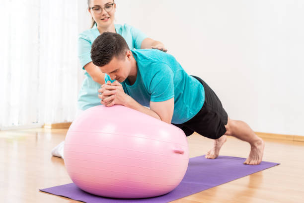 Physiotherapist working with young male client on core strength using fitball. Rehabilitation and physiotherapy background. stock photo