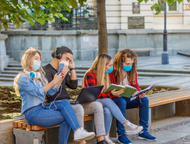 istock Beautiful Students are Working on a Laptop in Public Park with Preventive Measures due to Coronavirus. 1323448763