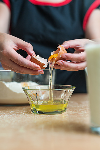 Close-Up View of Female Chef Breaking an Egg into a Glass Bowl in the Kitchen.