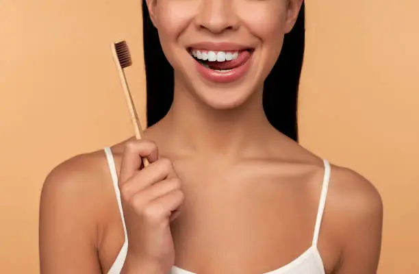 Young Asian woman in white lingerie with a toothbrush and white teeth on a beige background. Dental hygiene concept. Dentistry.