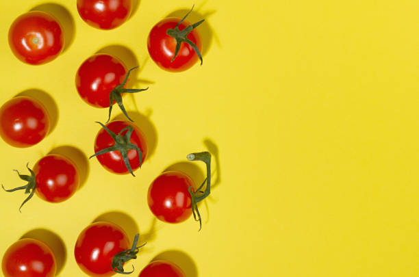 istock Juicy red tomato with green tail and shadow on yellow background, border, copy space, top view. Modern food pattern. 1323453059