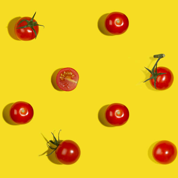 istock Summer food seamless pattern - red cherry tomatoes whole and sliced in sunlight with shadows on yellow background, flat lay. 1323453535