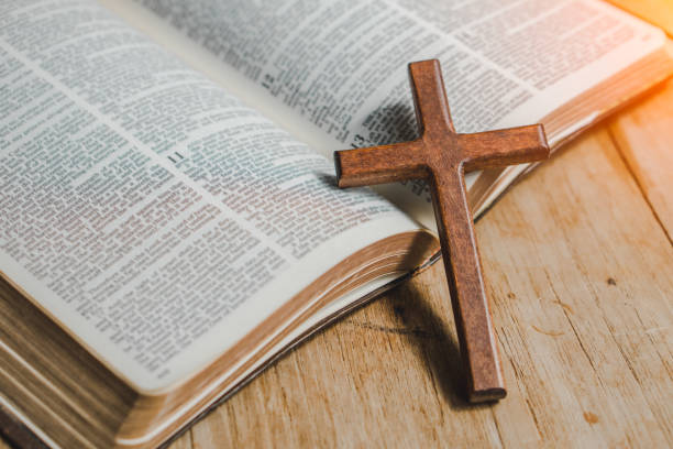istock the cross over opened bible on wood table with window light. 1323455276