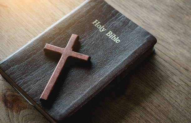 istock the cross over the bible on wood table with window light.christian backgound 1323455714