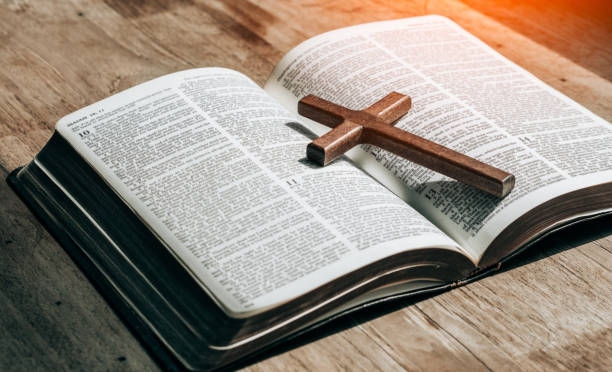 istock the cross over opened bible on wood table with window light.christian backgound 1323455797