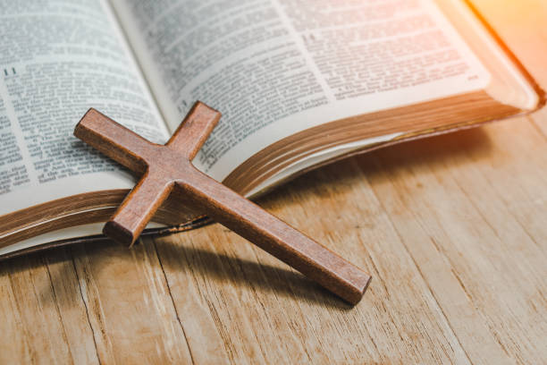 istock the cross over opened bible on wood table with window light. 1323456317