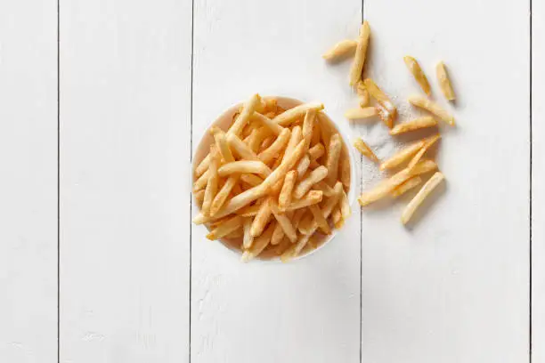 Photo of Crispy french fries in bowl on white wooden background