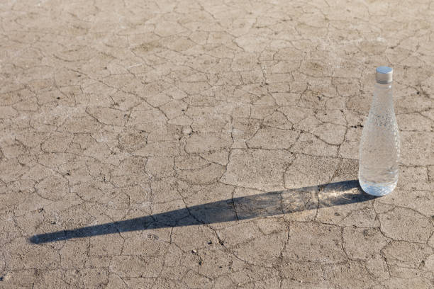 istock a bottle of drinking water stands on dry ground, casts a long shadow 1323461542