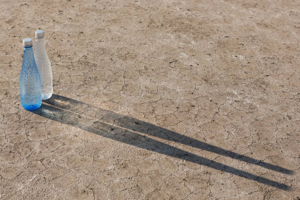 istock two bottles of drinking water stand on dry ground with cracks, cast a long shadow, concept 1323461573