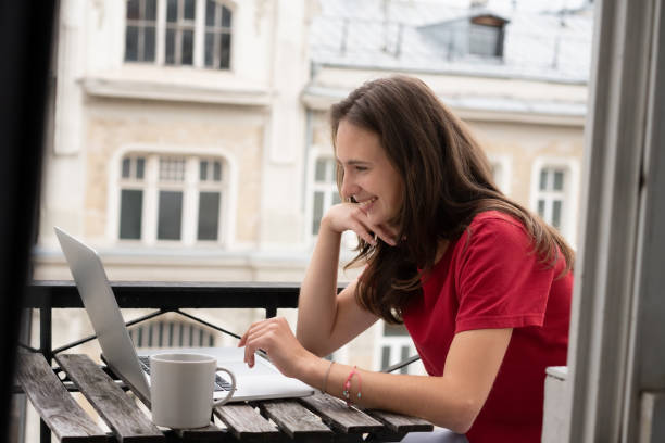 istock Beautiful young brunette woman sitting on balcony using laptop while having online chat consultation 1323463745
