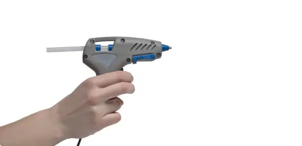 Gray electric glue gun in a female hand on a white background with place for text.